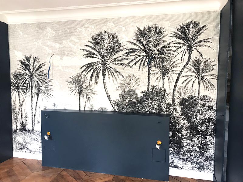 Tête de lit dans une chambre devant un poster mural avec des palmiers